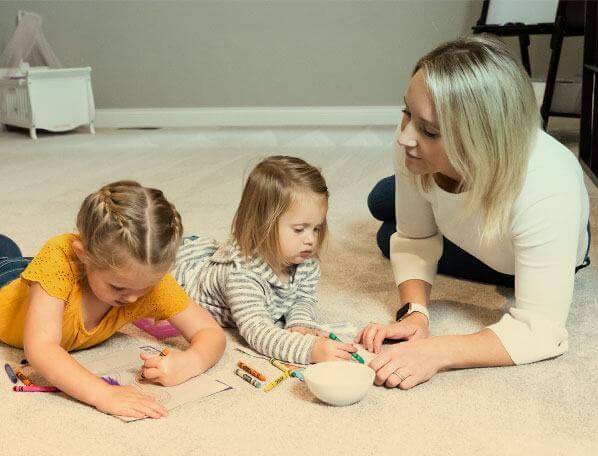 A mother with her children coloring in coloring books on the carpet